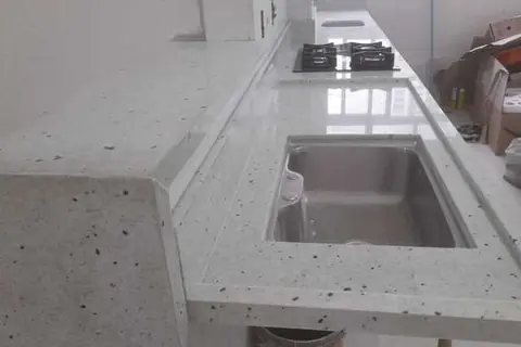 Bancada em granito claro com cuba de inox e cooktop - trabalho da Marmoraria Ita em Praia Grande